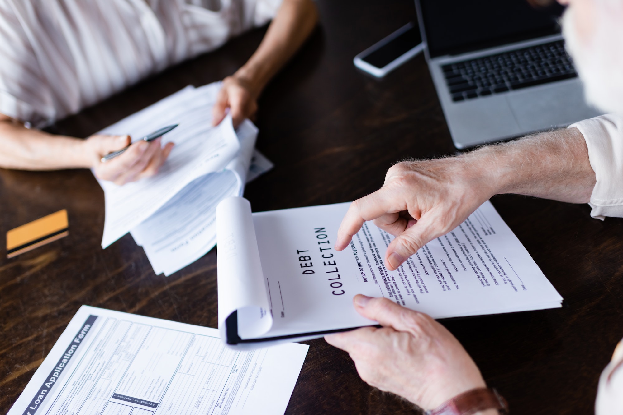 Cropped view of senior man pointing at paper with debt collection lettering near gadgets and wife at